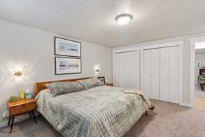 Bedroom with two closets, carpet flooring, baseboards, and a textured ceiling