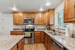 Kitchen featuring stainless steel appliances, a sink, a textured ceiling, light wood-type flooring, and light stone countertops
