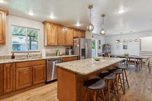 Kitchen with appliances with stainless steel finishes, a sink, light wood-style flooring, a kitchen bar, and a kitchen island