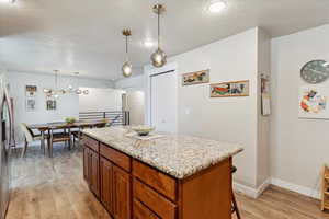 Kitchen featuring light wood-style floors, a textured ceiling, a kitchen island, baseboards, and light stone counters