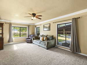 Carpeted living room featuring ceiling fan, crown molding, and a textured ceiling
