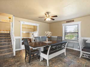 Dining room featuring a textured ceiling, wainscoting, a ceiling fan, stairs, and stone finish flooring