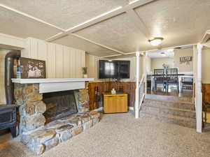 Carpeted living area featuring a textured ceiling, wood walls, a wainscoted wall, a wood stove, and a fireplace