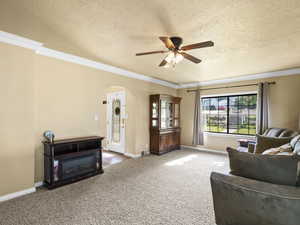 Carpeted living area with ceiling fan, arched walkways, ornamental molding, and a textured ceiling