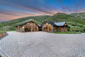 Rustic home featuring stone siding, a standing seam roof, an attached garage, and curved driveway