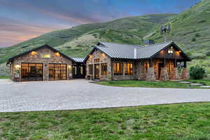 View of front of home with a standing seam roof, stone siding, an attached garage, and decorative driveway