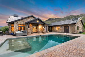 Rear view of house featuring a standing seam roof, a hot tub, a patio area, and stone siding