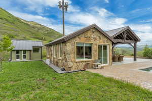 Rear view of property featuring stone siding, a patio area, a mountain view, and a lawn