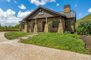Craftsman-style house with a standing seam roof, stone siding, a chimney, metal roof, and a front yard