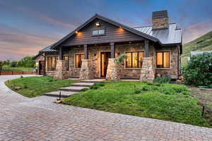 Craftsman house with a standing seam roof, a chimney, stone siding, metal roof, and a front yard