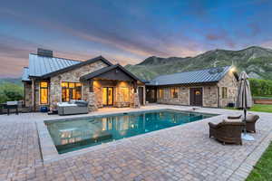 Pool at dusk with a patio area, an outdoor pool, a mountain view, and a hot tub