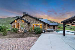 View of front of property with an outdoor hot tub, a standing seam roof, stone siding, and a patio area