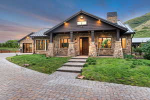 View of front facade with stone siding, a chimney, a standing seam roof, decorative driveway, and a lawn
