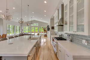 Kitchen featuring wall chimney exhaust hood, a chandelier, vaulted ceiling, a spacious island, and light wood-style floors