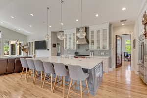 Kitchen featuring wall chimney range hood, backsplash, light wood-type flooring, recessed lighting, and white cabinetry
