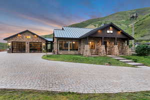 View of front facade featuring stone siding, a standing seam roof, decorative driveway, a garage, and a lawn