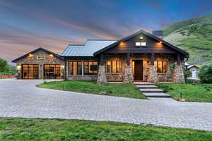 View of front facade with stone siding, decorative driveway, an attached garage, a yard, and a standing seam roof