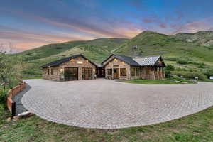 View of front of property with stone siding, a standing seam roof, a garage, a mountain view, and curved driveway