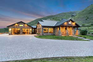 View of front of house featuring a standing seam roof, stone siding, a garage, and decorative driveway