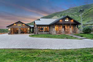 View of front facade with a standing seam roof, stone siding, decorative driveway, a garage, and a front lawn