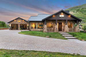 View of front of property with stone siding, decorative driveway, a lawn, a standing seam roof, and an attached garage