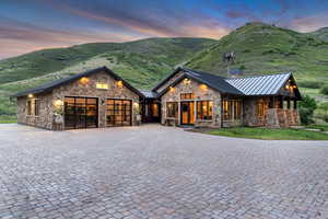 View of front facade featuring a standing seam roof, stone siding, a garage, and decorative driveway