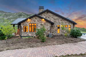 View of front facade featuring stone siding, a chimney, a standing seam roof, and central air condition unit