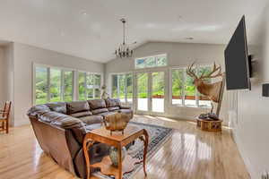 Living room with lofted ceiling, light wood-type flooring, french doors, a chandelier, and baseboards
