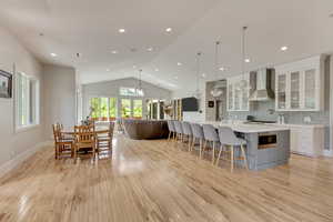 Kitchen featuring wall chimney exhaust hood, a chandelier, light wood-type flooring, light countertops, and lofted ceiling