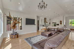 Living room with light wood-style flooring, lofted ceiling, a chandelier, baseboards, and recessed lighting