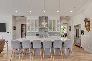 Kitchen with a chandelier, wall chimney exhaust hood, stainless steel built in fridge, decorative backsplash, and recessed lighting