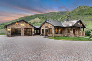 View of front of property featuring a standing seam roof, stone siding, an attached garage, metal roof, and a mountain view