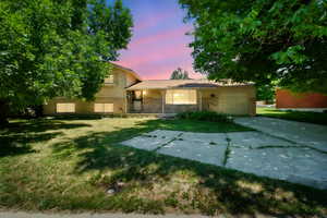 Split level home with brick siding, driveway, an attached garage, and a yard