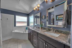 Full bath featuring double vanity, a garden tub, tile patterned flooring, a textured ceiling, and vaulted ceiling