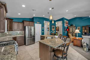 Kitchen with stainless steel appliances, lofted ceiling, open floor plan, light tile patterned flooring, and decorative backsplash