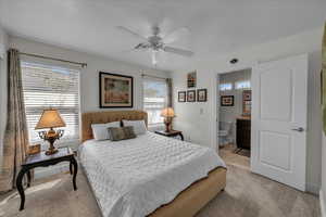 Bedroom with light colored carpet, multiple windows, connected bathroom, and a ceiling fan