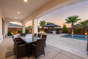 Patio terrace at dusk featuring a patio, outdoor dining area, a gazebo, a fenced backyard, and an outdoor living space with a fire pit