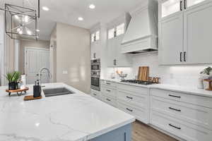 Kitchen featuring premium range hood, a chandelier, recessed lighting, decorative backsplash, and white cabinets
