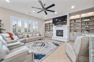 Living room with ceiling fan, light wood-style flooring, a glass covered fireplace, recessed lighting, and built in shelves