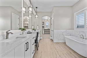 Ensuite bathroom featuring plenty of natural light, vanity, a soaking tub, and wood finished floors