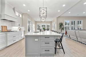 Kitchen with custom range hood, a chandelier, light wood finished floors, white gas stovetop, and recessed lighting