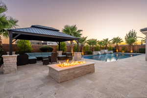 Pool at dusk featuring a gazebo, an outdoor living space with a fire pit, a patio area, and a fenced backyard