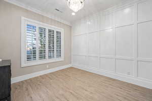 Empty room with crown molding, a decorative wall, a chandelier, and light wood-style floors