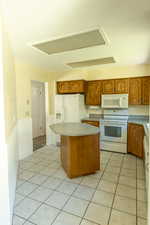 Kitchen featuring white appliances, brown cabinetry, a kitchen island, and light tile patterned floors