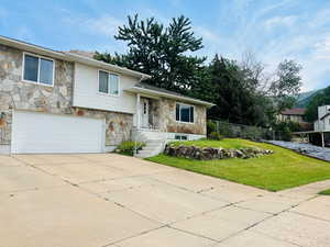 Tri-level home featuring stone siding, a garage, and driveway