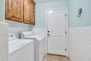 Laundry area featuring washing machine and clothes dryer, tile walls, cabinet space, a wainscoted wall, and light tile patterned flooring