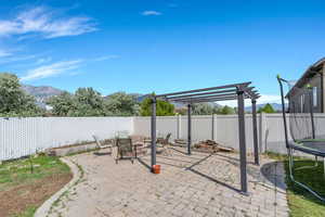 Fenced backyard with a trampoline, a patio area, a pergola, and a mountain view