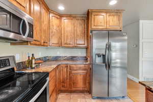 Kitchen featuring appliances with stainless steel finishes, brown cabinets, dark stone counters, and recessed lighting