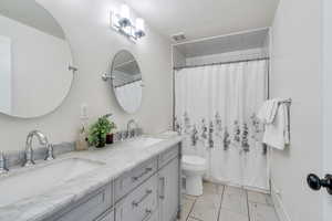 Bathroom featuring marble finish floors, double vanity, and a shower with shower curtain