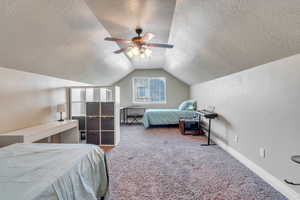 Bedroom featuring a textured ceiling, carpet, vaulted ceiling, and a ceiling fan